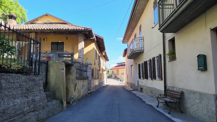 Forward camera movement down a quiet narrow residential village street in Piedmont, Italy.