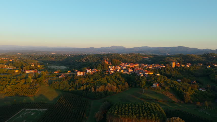 Compact rural settlement sits among green hills and farmland as the camera flies past in warm evening light.