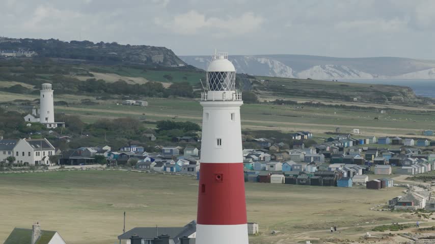 Telephoto view of Portland Bill Lighthouse with the Old Lower Lighthouse coastal landscape and distant Dorset cliffs on the Isle of Portland England