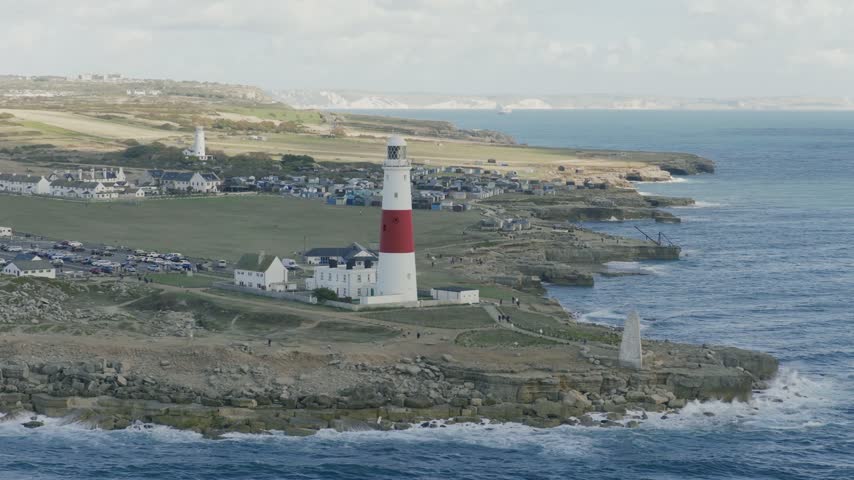 Telephoto view of Portland Bill Lighthouse on the Isle of Portland in Dorset England with rocky coastline surrounding sea and the wider coastal landscape behind