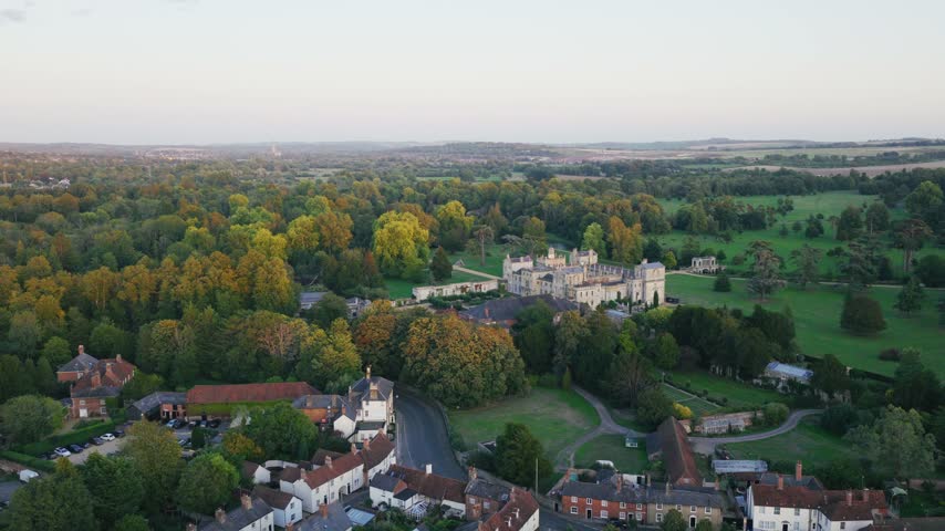 Wide aerial view of historic Wilton House in Wiltshire England surrounded by landscaped parkland mature trees autumn colours gardens and nearby village buildings