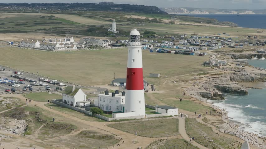 Telephoto view of Portland Bill Lighthouse on the Isle of Portland in Dorset England with the Old Lower Lighthouse coastal buildings rocky shoreline and surrounding landscape
