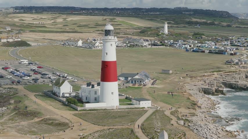 Telephoto view of Portland Bill Lighthouse on the Isle of Portland in Dorset England with the Old Lower Lighthouse coastal landscape rocky shoreline and surrounding buildings behind