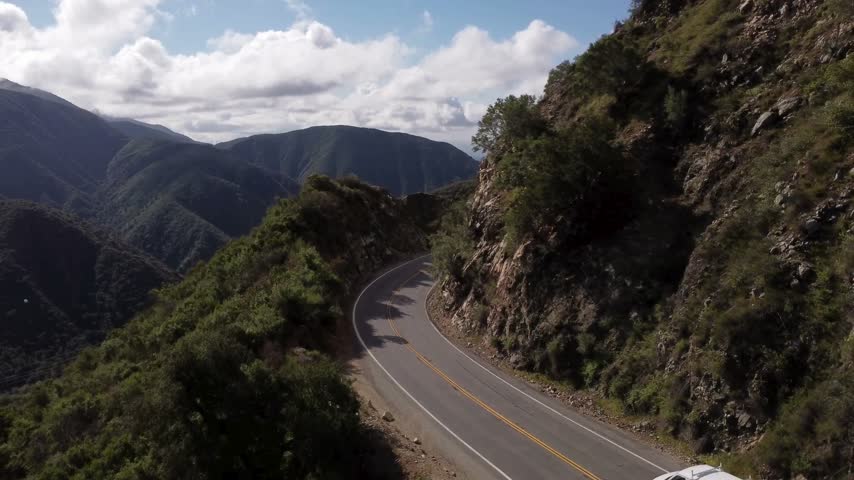 Winding Mountain Road Through Green Hills Under Cloudy Sky