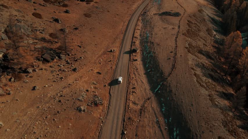 Aerial drone shot of a vehicle traveling on a remote dirt road in autumn.
