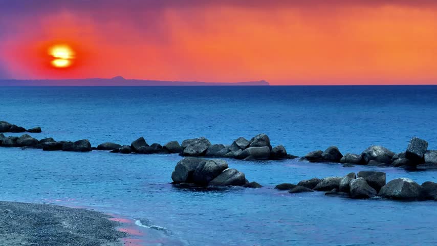 Sunset over the Mediterranean Sea seen from the Sicilian coast with the sky turning orange and in the distance the outline of the promontory of Capo Milazzo