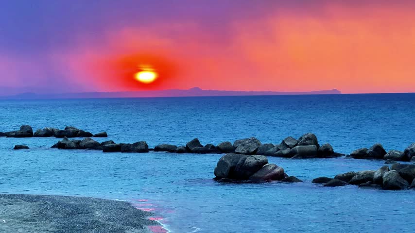 Sunset over the Mediterranean Sea seen from the Sicilian coast with the sky turning orange and in the distance the outline of the promontory of Capo Milazzo