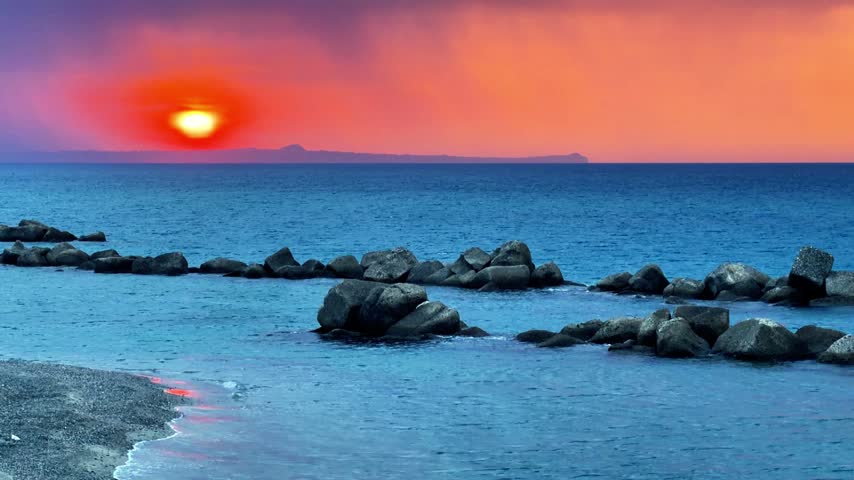Sunset over the Mediterranean Sea seen from the Sicilian coast with the sky turning orange and in the distance the outline of the promontory of Capo Milazzo
