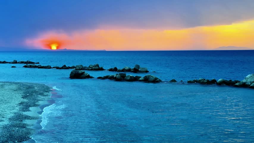 Sunset over the Mediterranean Sea seen from the Sicilian coast with the sky turning orange and in the distance the outline of the promontory of Capo Milazzo
