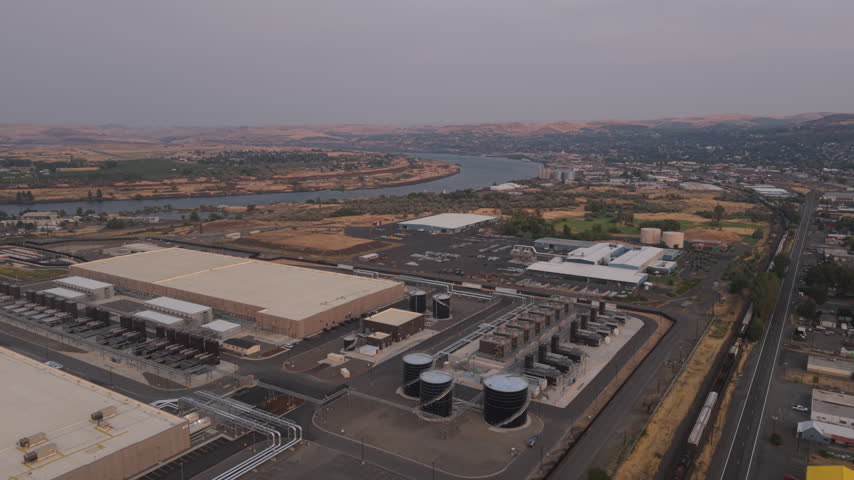 Large data center in The Dalles, Oregon, with a freight train passing beside the technology campus, combining digital industry, rail logistics and industrial development.