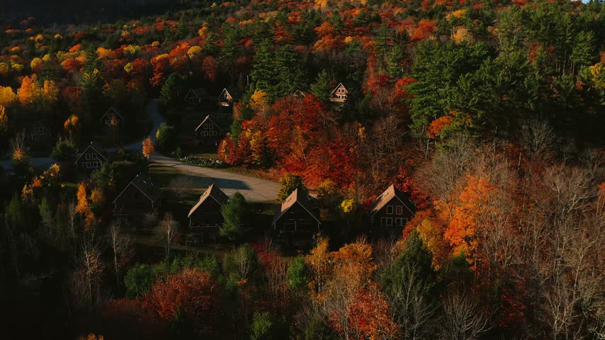 Warm New England sunset over New Hampshire fall foliage with a cozy cottage nestled in the forest