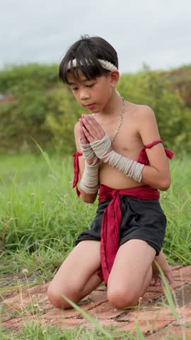 A young Muay Thai fighter performs the traditional Wai Kru ritual kneeling outdoors in Ayutthaya.