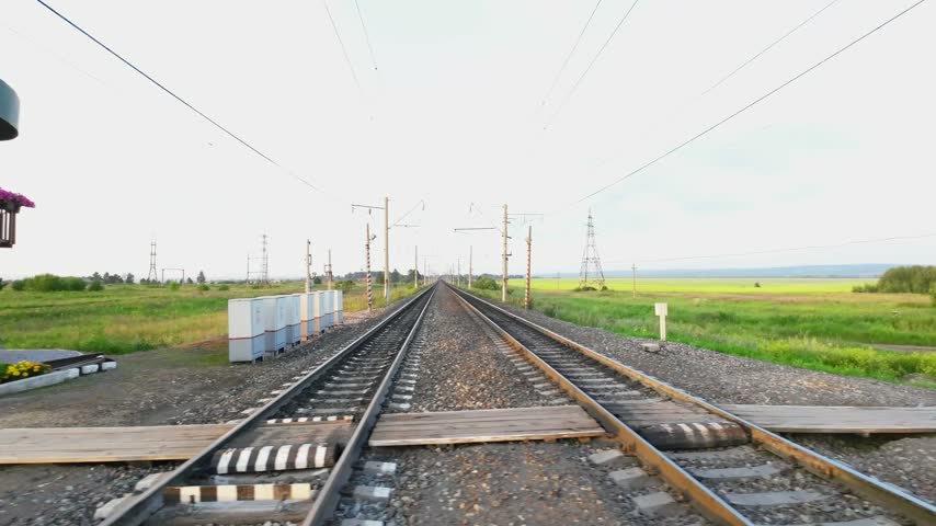 Scenic perspective of a railroad crossing with tracks extending into the horizon, captured from inside a moving vehicle.