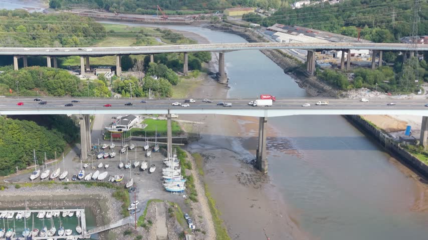 Aerial View of Busy M4 Motorway Overpass on River Neath with Docked Boats and Industrial Buildings Below.