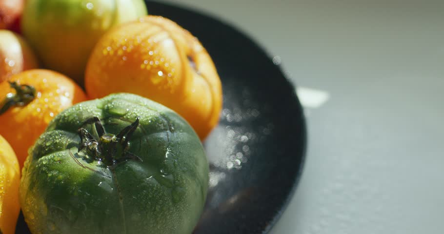 Yellow, green and red tomato on a dark plate. Tomatoes sprinkled with water. Agricultural industry and farming.	

