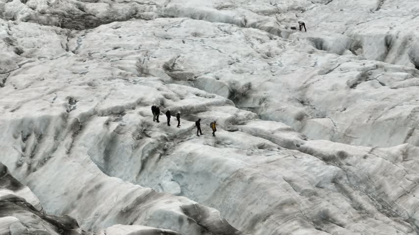 An aerial drone pan right and tracking shot follows a group of hikers exploring the vast, rugged ice formations and crevasses of Falljökull glacier on Iceland.