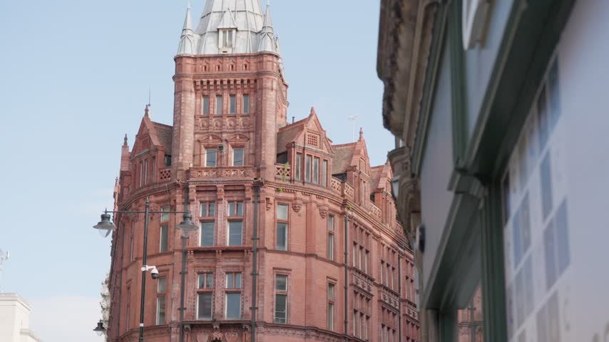Ornate red brick Victorian corner building with a spire against blue sky.