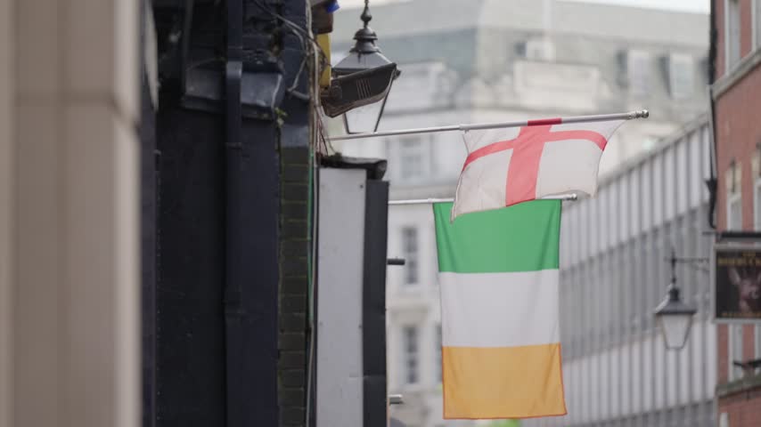 Green, white and orange flag hangs from a building above a city street.