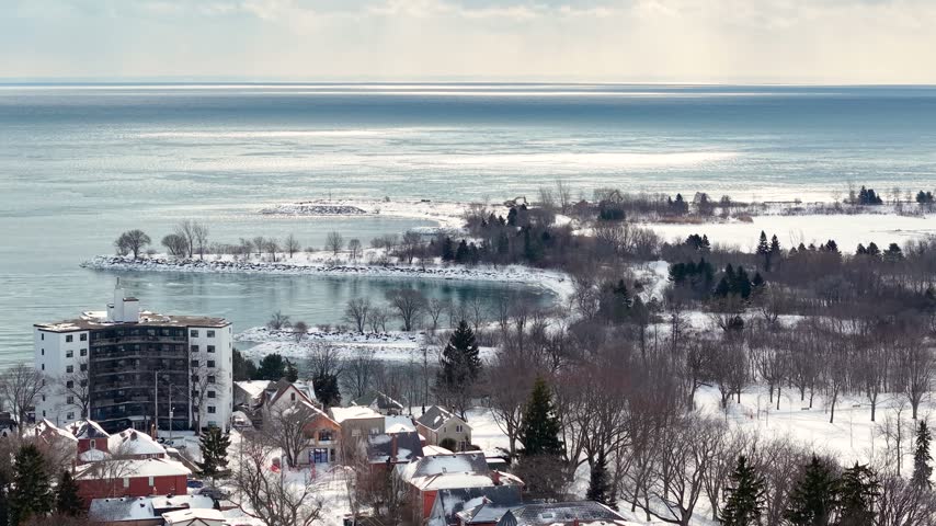 Aerial view of snow covered waterfront trees and residential buildings beside the lake in Toronto Ontario Canada during winter