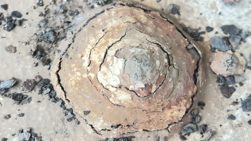 A detailed close up view of a weathered metal structure displaying circular layers of rust and oxidation, showing deep cracks and textured decay on a damaged industrial surface.