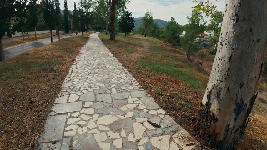 First-person perspective walking from a paved sidewalk onto a dirt path in a rural park