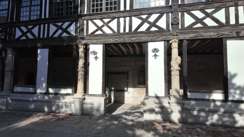 Half-timbered gallery at Aître Saint-Maclou in Rouen, France with carved wooden beams, stone columns, white plaster panels and shaded courtyard