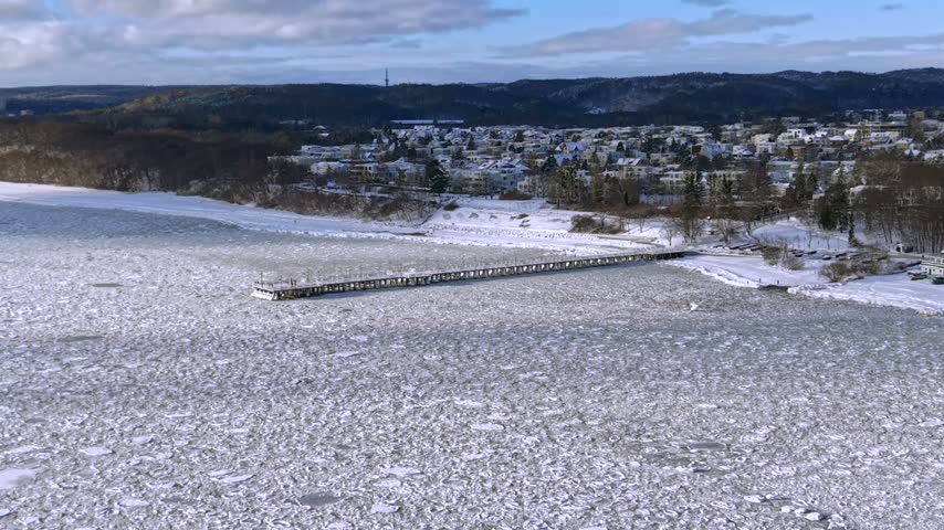 Aerial drone shot of the Orłowo pier over the frozen Baltic Sea looking toward the snowy shore and the city of Gdynia in winter, Poland