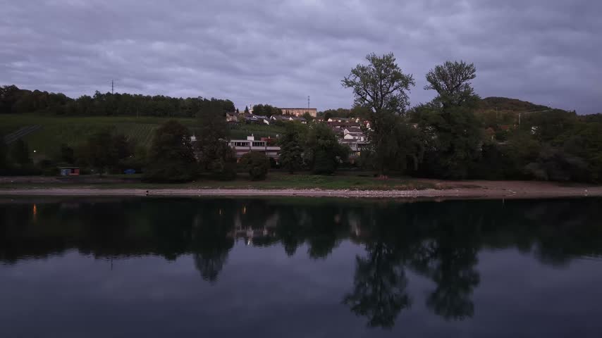 Aerial view of Schaffhausen, Switzerland, at dusk, showing vineyards on green hillsides, residential houses, trees and the Rhine River beneath a cloudy evening sky.