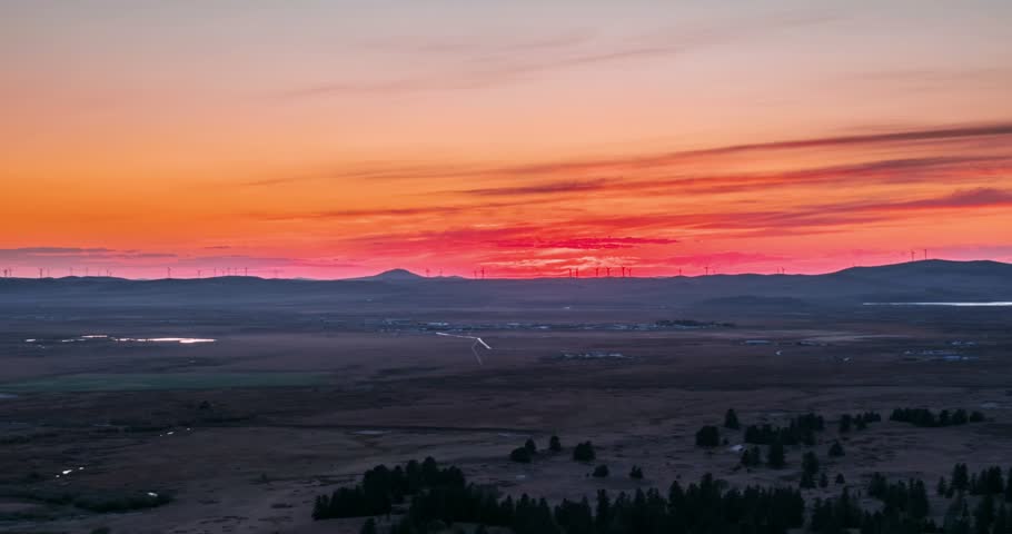 Aerial time-lapse of a fiery red sunset over grassland wind turbines in Inner Mongolia, China, streaked clouds glowing above dark hills and wetland pools.