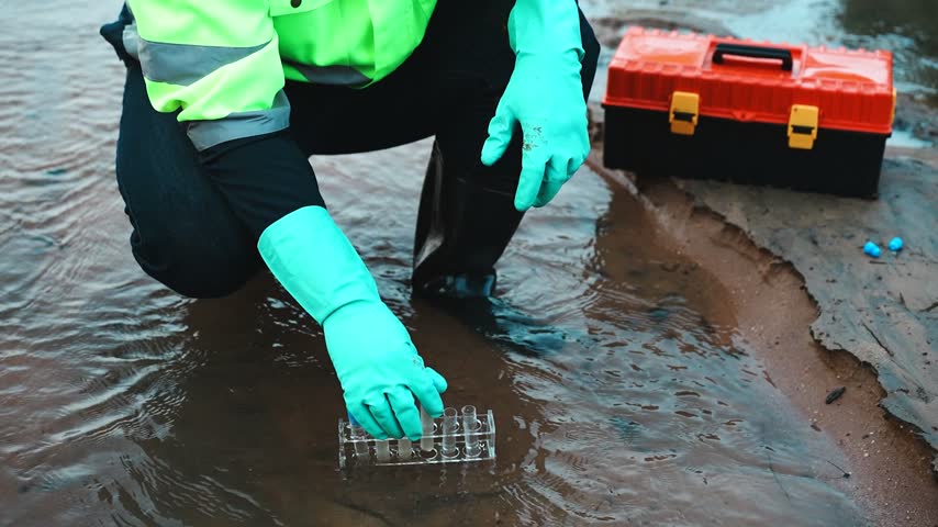 A field researcher carefully seals a test tube containing a water sample collected from a natural water source, preparing it for laboratory analysis.