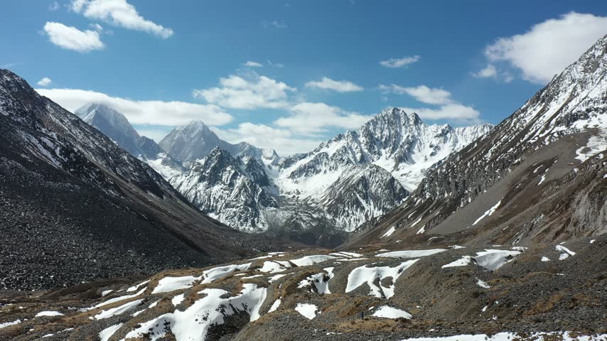 Drone video of Gongga mountain range in Sichuan, China, featuring majestic snowy peaks, glaciers, and a valley with a small lake, filmed from an aerial perspective.