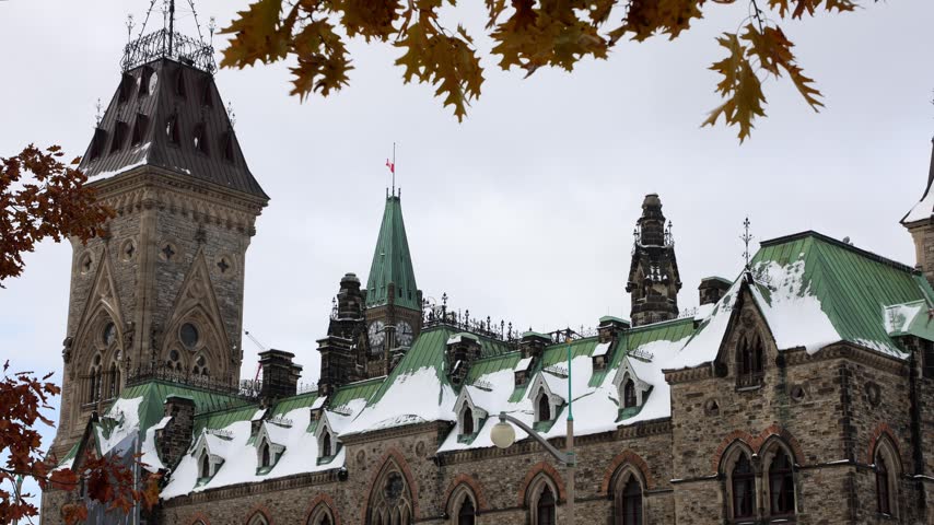 West Block Parliament building with snow covered roofs framed by fall foliage
