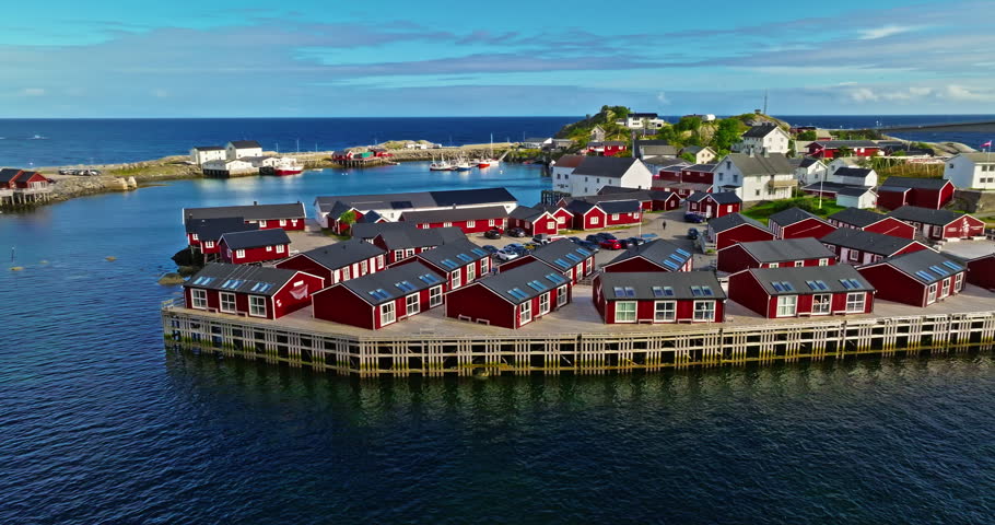 Aerial view of traditional red fishing cabins of Hamnoy in Lofoten, Norway. Massive rocky mountain peaks tower above historic Norwegian village. Red houses