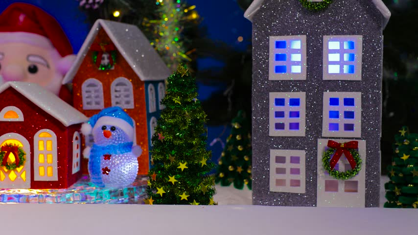 An orange car drives past colorful little houses with bright lights in their windows, set in a Christmas town