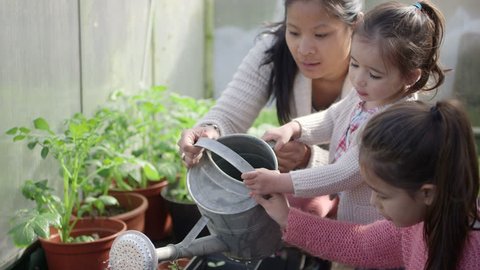 Mother teaching daughters in greenhouse
