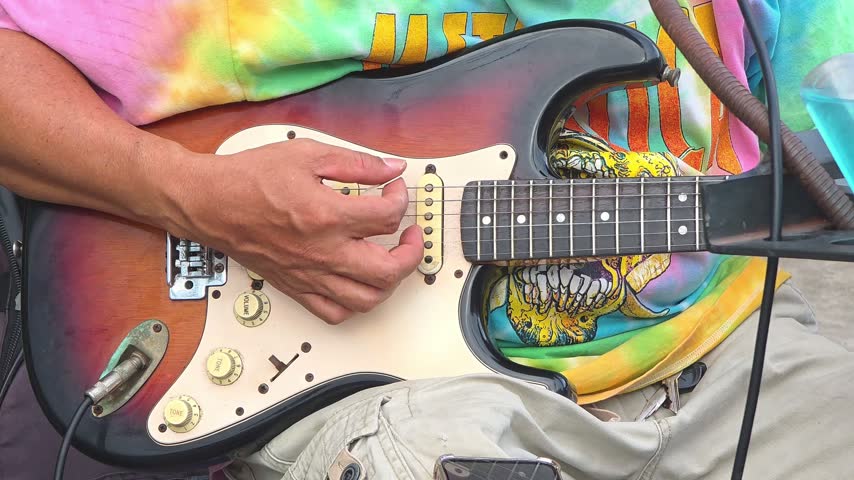 street musician playing sunburst electric guitar close up on hands plucking strings

