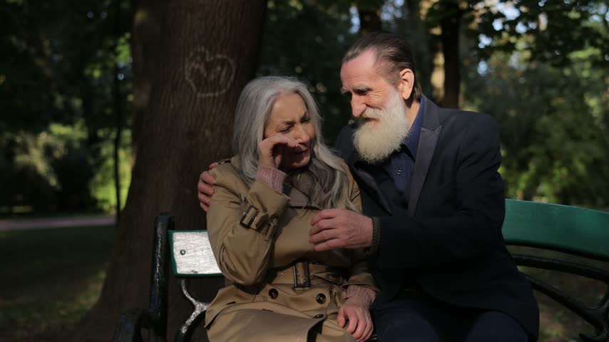 Elderly couple sitting on park bench talking and hugging