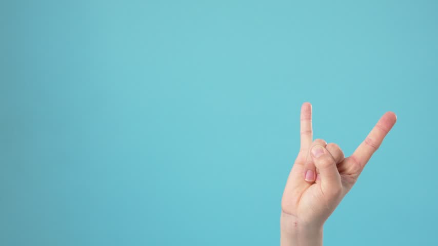 A human hand makes the rock on sign against a plain light blue background. The hand moves rhythmically, gesturing energy, music enthusiasm, and heavy metal culture in a clean studio setting.