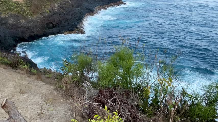 Ocean waves crashing against volcanic rocks along scenic coastal cliff in Bali
