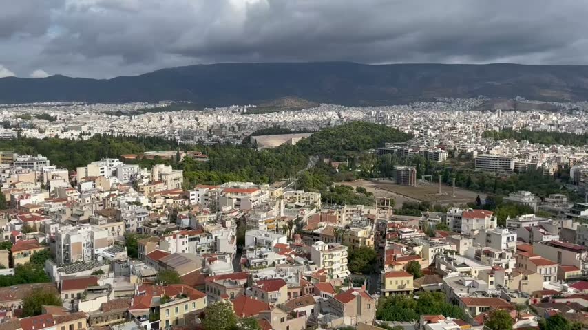 Panoramic view of Athens, Greece, from the Acropolis near the Parthenon. The expansive cityscape features dense urban rooftops, historic surroundings and the mountainous landscape beyond the Greek capital. Travel footage of Athens and its distinctive Mediterranean urban landscape.