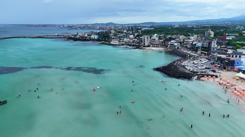 Aerial view of people enjoying a summer day at hyeopjae beach on jeju island, south korea. The turquoise water gently laps the shore