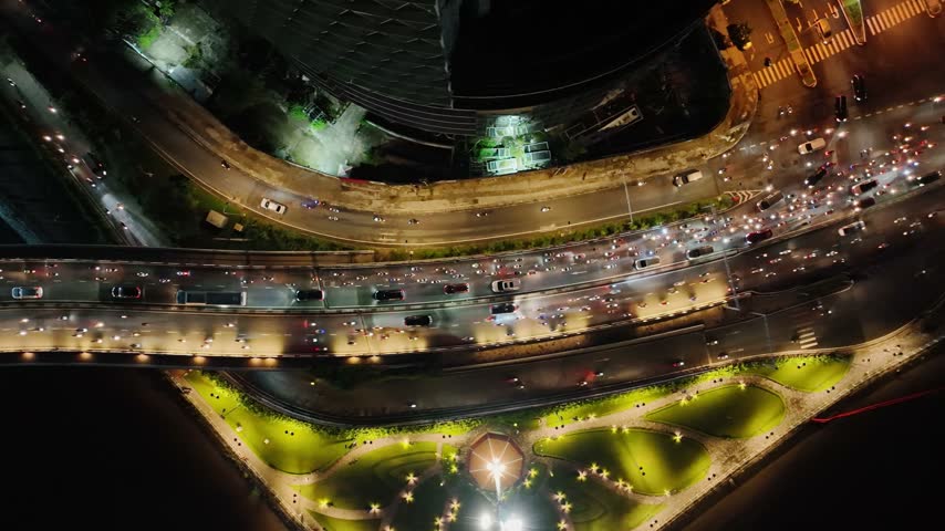 Top down aerial view of illuminated roads and moving traffic beside the river at night in Ho Chi Minh City, Vietnam, showing curved roadways.
