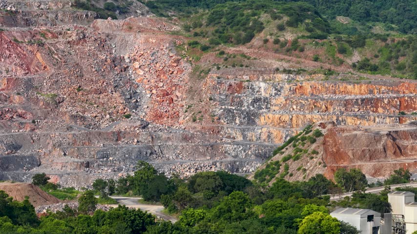 Sunlit open pit limestone quarry with terraced rock cliffs and lush green trees.