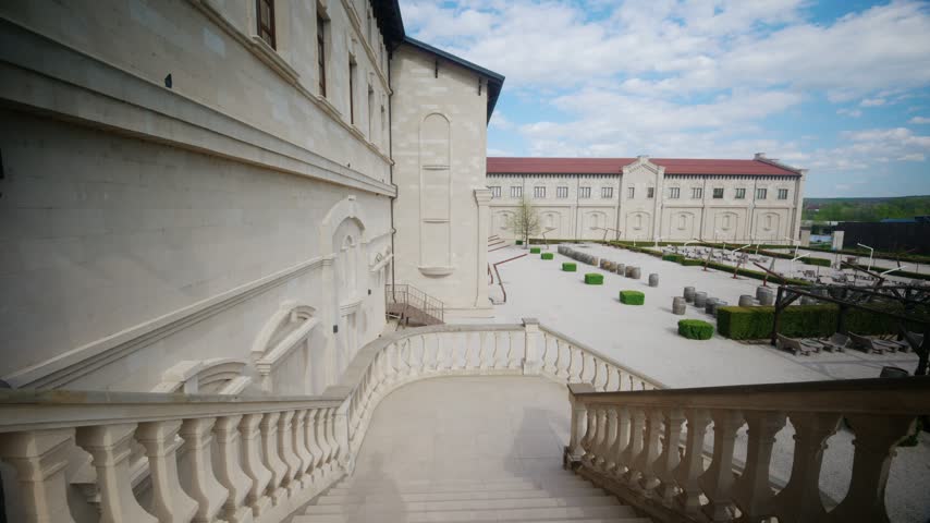 Grand stone staircase descending into a spacious landscaped winery courtyard with oak barrels under a clear blue sky.