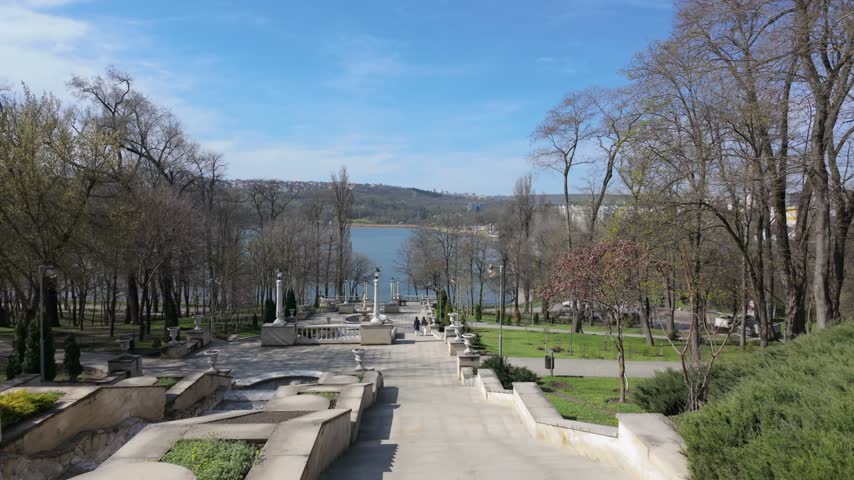 Slow motion descent down stone staircase in public park with classical architecture landscape view of lake and forest.