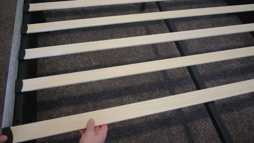 Person assembling wooden slats on a bed frame
