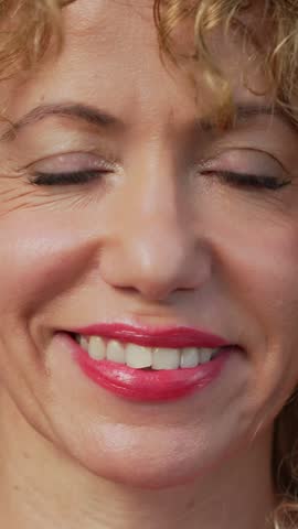 Mature blonde woman with curly hair and green eyes smiling at the camera in a close up shot