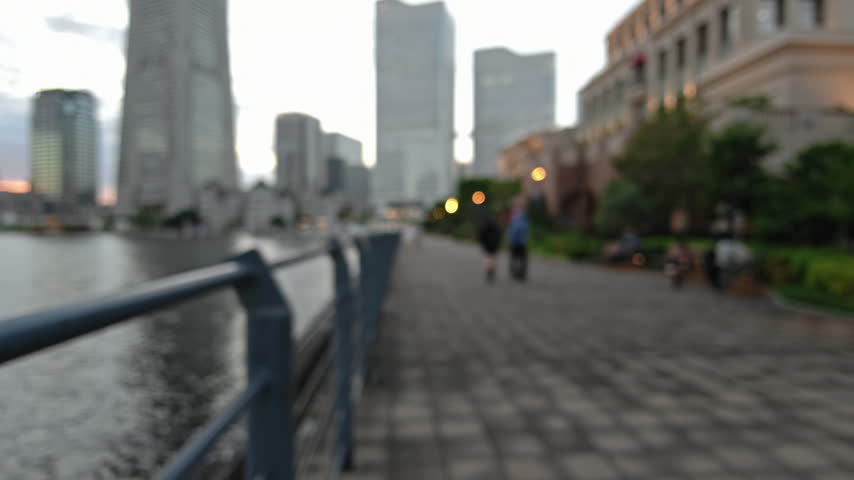 Blurred background of waterfront promenade city skyline railing dusk urban walkway beside calm reflective water in Yokohama, Japan