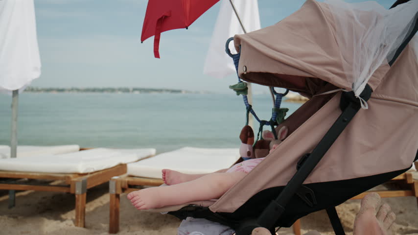 Baby sitting in stroller under bright red beach umbrella by the sea