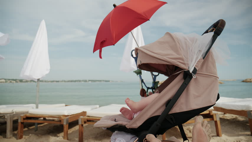 Baby sitting in stroller under bright red beach umbrella by the sea